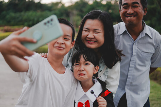 Asian young child wear a graduation gown and family take group photos to capture memories of important life events with happy face, make silly faces taking selfies.Concept of family and  graduate day.