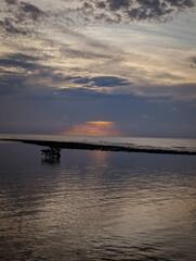 The image shows a sunset over the water. The sky is dominated by scattered clouds, with shades of blue, gray, and a little orange near the horizon. 