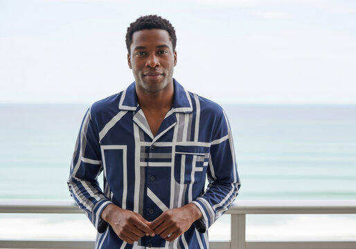 Young black man in striped day-jama with geometric lines standing on balcony with ocean view