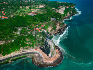 Aerial view of Pura Luhur Uluwatu Temple, Bali and the Emerald Coast in the summer sun. Construction equipment reinforces the rock