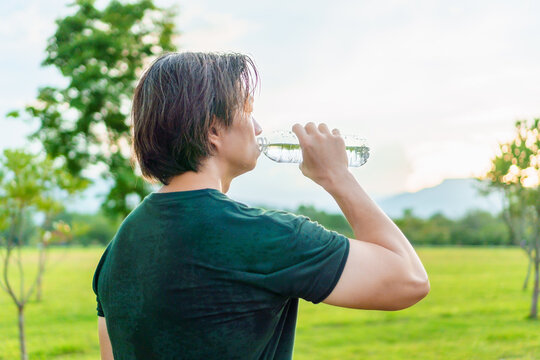 Athlete drinking water from a bottle after running in park, outdoor workout with warm light of sunset on freshy green of nature  background. Thirsty runner and bottle for hydration, electrolytes. - Powered by Adobe