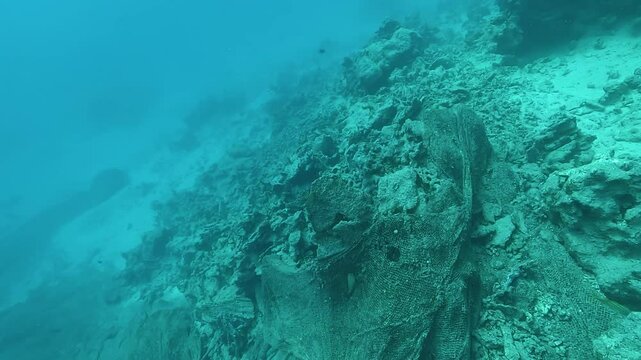 Old fishing nets lying on the sandy seabed beside a sunken trawler. Underwater shot showing marine pollution. Check my portfolio for more shipwreck footage.