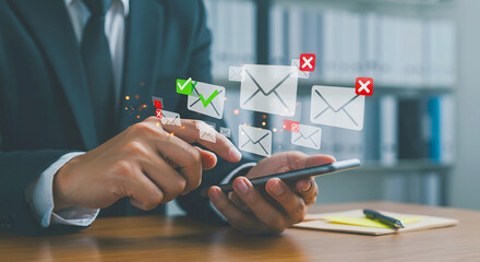 Person in suit using smartphone with email icons floating above it on a desk with office supplies