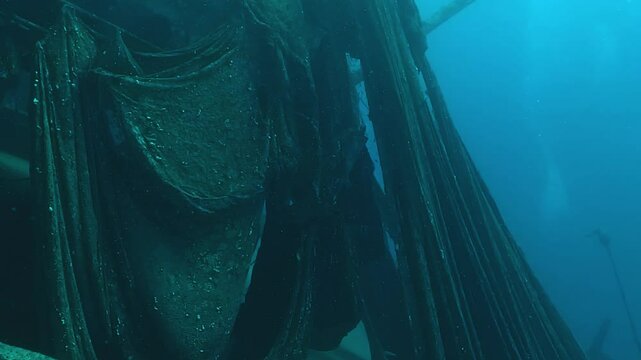 Side view of a sunken trawler covered in shredded ghost nets, slowly releasing plastic into the ocean. Underwater tracking shot. Check my portfolio for more shipwreck footage.