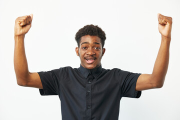 Excited black man celebrating victory with raised arms, joyful expression, wearing a black shirt, positive energy radiates in bright setting.