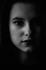 Black and white portrait of a young beautiful dark-haired girl in a low key.