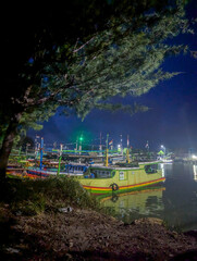 Fototapeta premium night view on the edge of a river or small harbor with the main focus on the fishing boats anchored. The pitch-black sky indicated deep night.