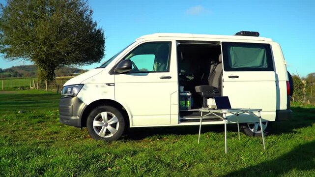 Campervan Opens its Doors to Display a Makeshift Office Setup in a Green Field, with a focus on the freedom and flexibility of remote work.