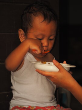 A young Javanese boy, about two years old, diligently learning to eat with a spoon. A candid portrait of a key childhood milestone in Central Java, Indonesia.