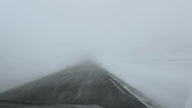 Foggy road with low visibility and snow on asphalt, disappearing into thick mist creating quiet winter atmosphere