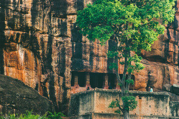 Ancient rock-cut caves carved into reddish cliffs at Badami. Visitors nearby add a sense of scale...