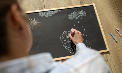 girl draws flower and sun with colored chalk on black board. simple children's drawing on black...
