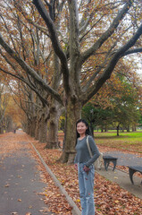 a happy chinese woman standing on fallen leaves in Flushing Meadows Corona Park