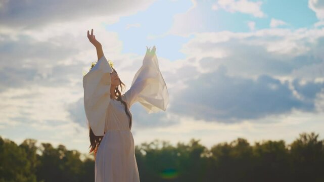 in silhouette portrait real person happy young woman pray hands folded in prayer raised to blue sky to divine sun light green forest trees. Fantasy girl enjoy summer nature. herbal wreath white dress