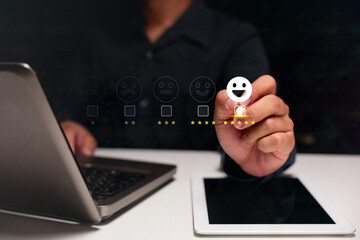 A person rates a service by selecting a happy face emoji on a virtual feedback scale above a laptop and tablet.