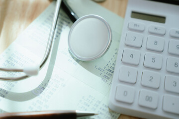 A stethoscope head lies on financial documents, alongside a calculator and coins, suggesting...