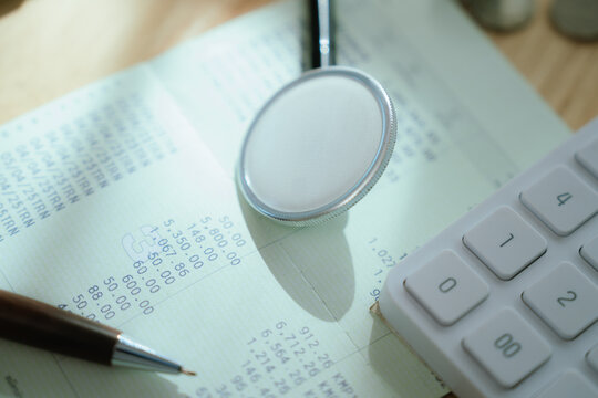 A stethoscope head lies on financial documents, alongside a calculator and coins, suggesting healthcare cost analysis.