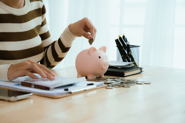 An Asian woman is putting money in a piggy bank while looking at a calculator, giving advice on financial planning.