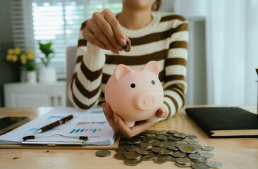 An Asian woman is putting money in a piggy bank while looking at a calculator, giving advice on financial planning.