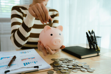 An Asian woman is putting money in a piggy bank while looking at a calculator, giving advice on financial planning.