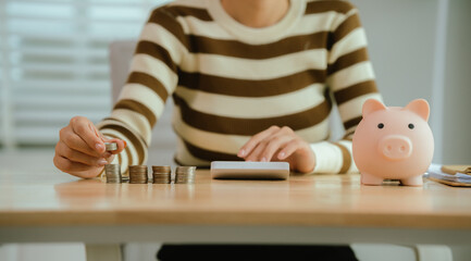 An Asian woman is putting money in a piggy bank while looking at a calculator, giving advice on...