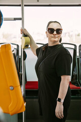 Confident woman in a black outfit holding a pole inside a modern bus. A perfect image for illustrating urban lifestyle, commuting, independence, and public transport concepts.