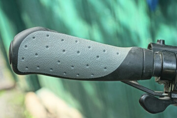 part of the bike from a metal handlebar with a plastic gray black  handle and a brake with a cable on the street