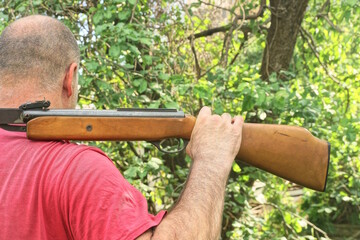 one man hunter in red clothes holds air rifle in hand on shoulder against green vegetation...