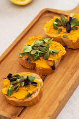 Delicious bruschetta with pumpkin hummus and microgreens on wooden board