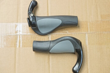 two new gray black plastic bicycle handles lie on brown table