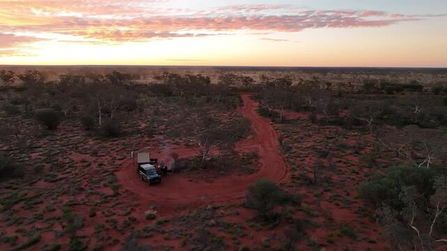 Cinematic Drone Orbit of Remote Outback Campsite with Campfire and Dust Trail at Sunset