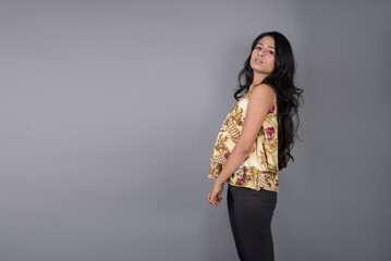 A charming young woman wearing a floral patterned top, black leggings and black heels, posing with...