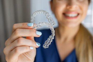 Smiling woman holding transparent dental aligner braces for orthodontic treatment
