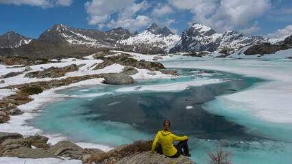 woman on the shore of the thawing lake with a view of the snow-capped mountains