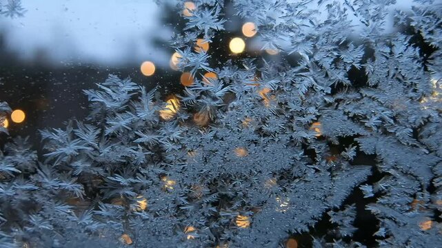 Frost patterns on holiday window with blurred lights outside  