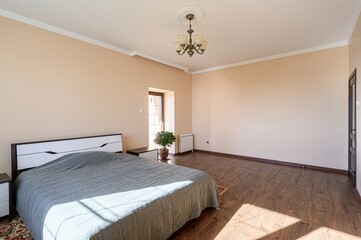 Bright bedroom with a bed, wooden floors, beige walls, and natural light coming through a window. A...