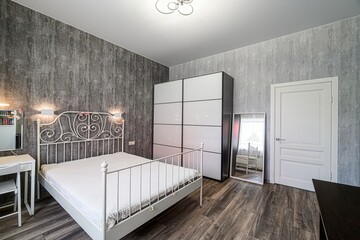 Cozy bedroom with a white iron bed, wardrobe, and neutral tones. Wood floors add warmth to the space