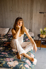 A woman in floral pajamas sits on a bed, lost in thought. Ideal for promoting slow living,...