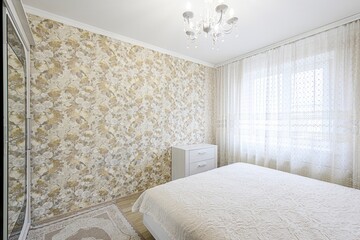 bright bedroom with floral wallpaper, a white bed, curtains, a chandelier, and a white dresser