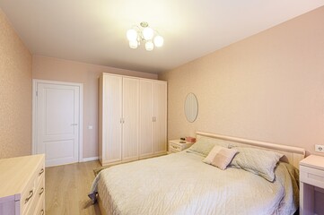 cozy bedroom with a bed, wardrobe, and dresser. The room features light beige walls, wooden floors,...