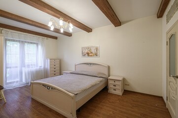 Bedroom with a light-colored bed, wooden beams, and natural light