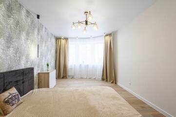 cozy bedroom features a brown bed, forest-themed wallpaper, neutral curtains, and light wood floors. A modern chandelier hangs above the bed
