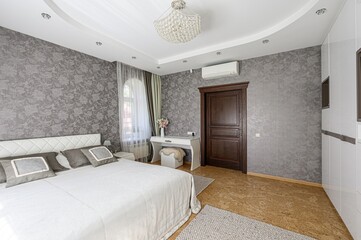 Elegant bedroom with floral wallpaper, white bed, crystal chandelier, and dark wood door