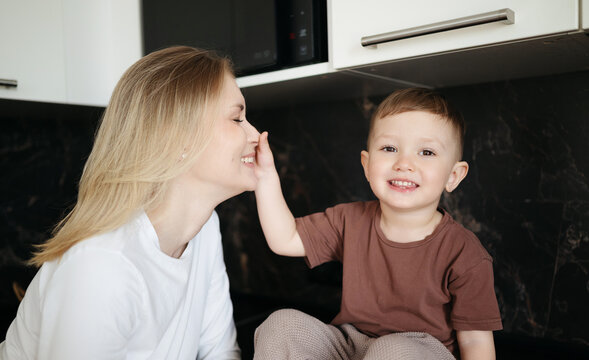 Little boy smiling while gently touching his mother's nose during a playful and affectionate moment in a modern kitchen at home.