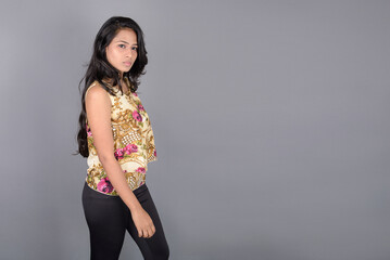 A charming young woman wearing a floral patterned top, black leggings and black heels, posing with...