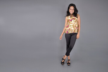 A charming young woman wearing a floral patterned top, black leggings and black heels, posing with...
