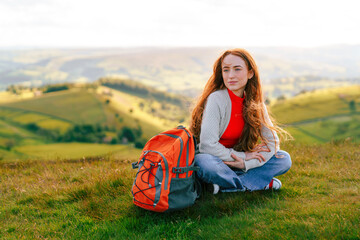 Woman sits on green hillside with backpack during golden hour capturing serene outdoor adventure...