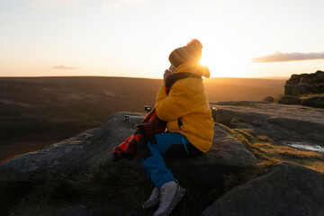 Sunset contemplation on a rocky outcrop in a vibrant yellow jacket during a cool evening in a serene landscape