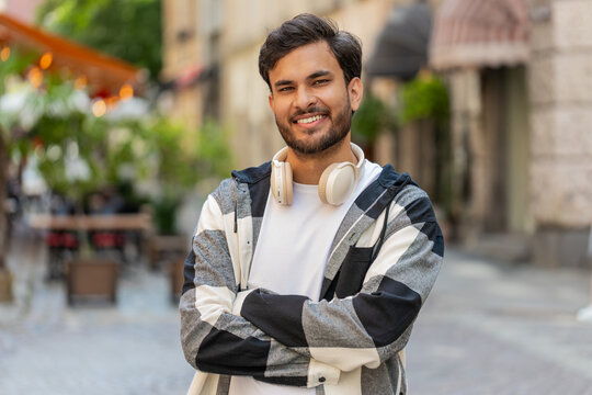 Portrait of happy smiling Indian young man turn face looking at camera, resting, relaxation feel satisfied glad expression of good news outdoors. Hispanic guy in urban city street. Town lifestyles.