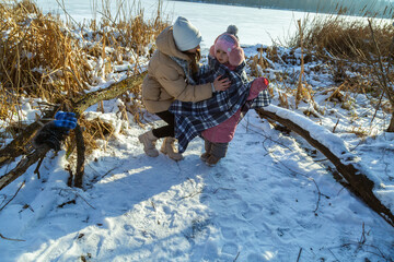 In winter, mother and daughters walking on the shore of the lake. Mom warms her daughter with a cover